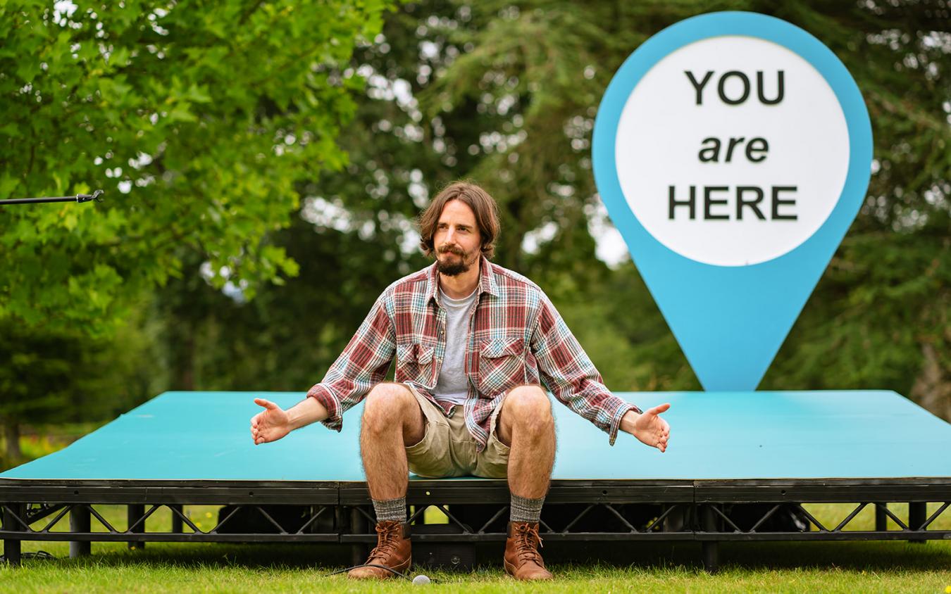 Photo of Harry Egan siting on the stage with You Are Here sign in background